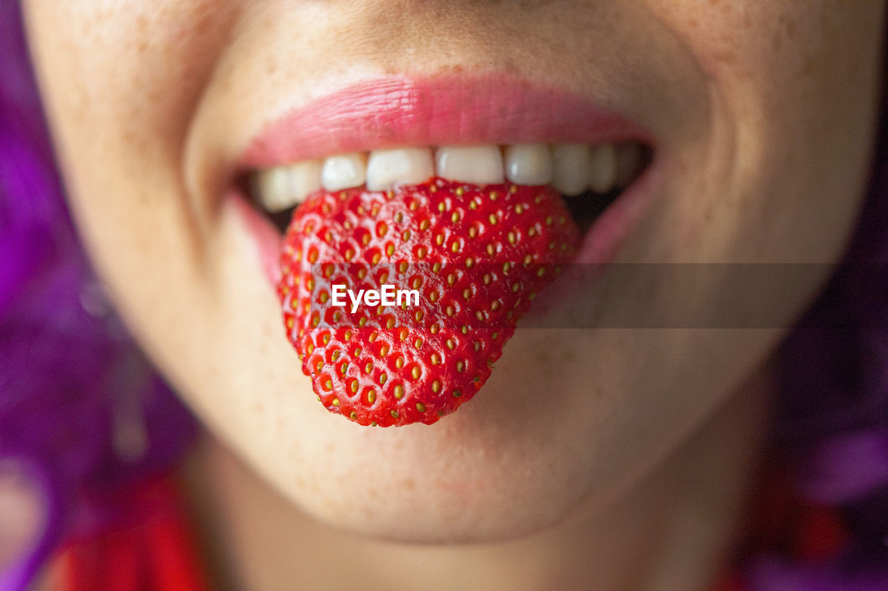 Close-up of woman face holding strawberry outdoors