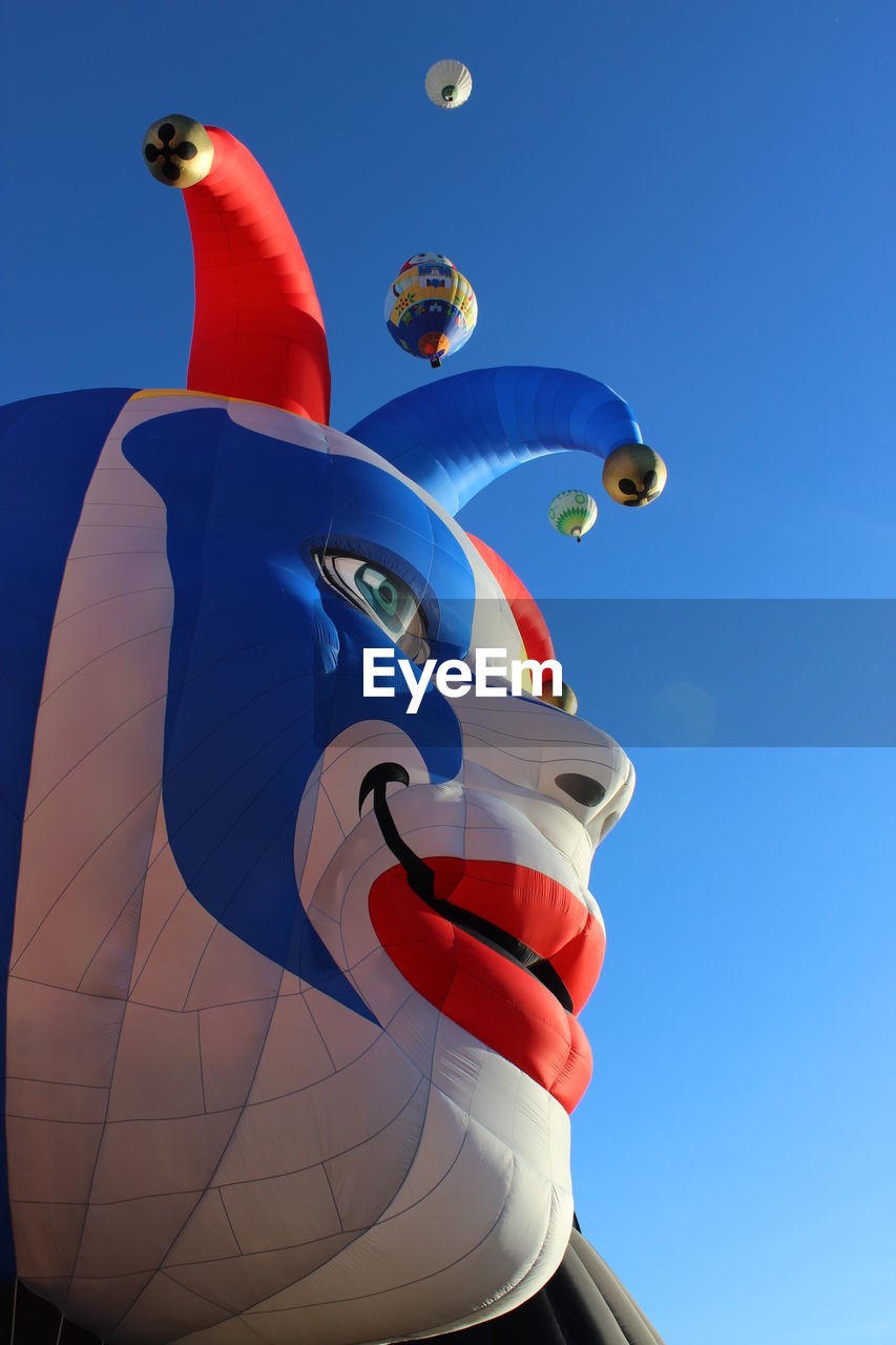 Low angle view of inflatable clown head against clear sky