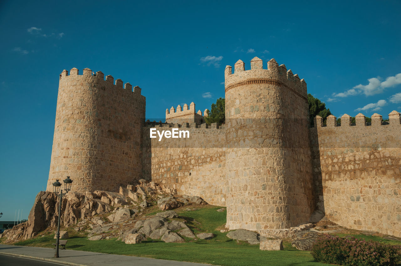 Street and light posts beside stone towers in the large wall encircling the town of avila, in spain.