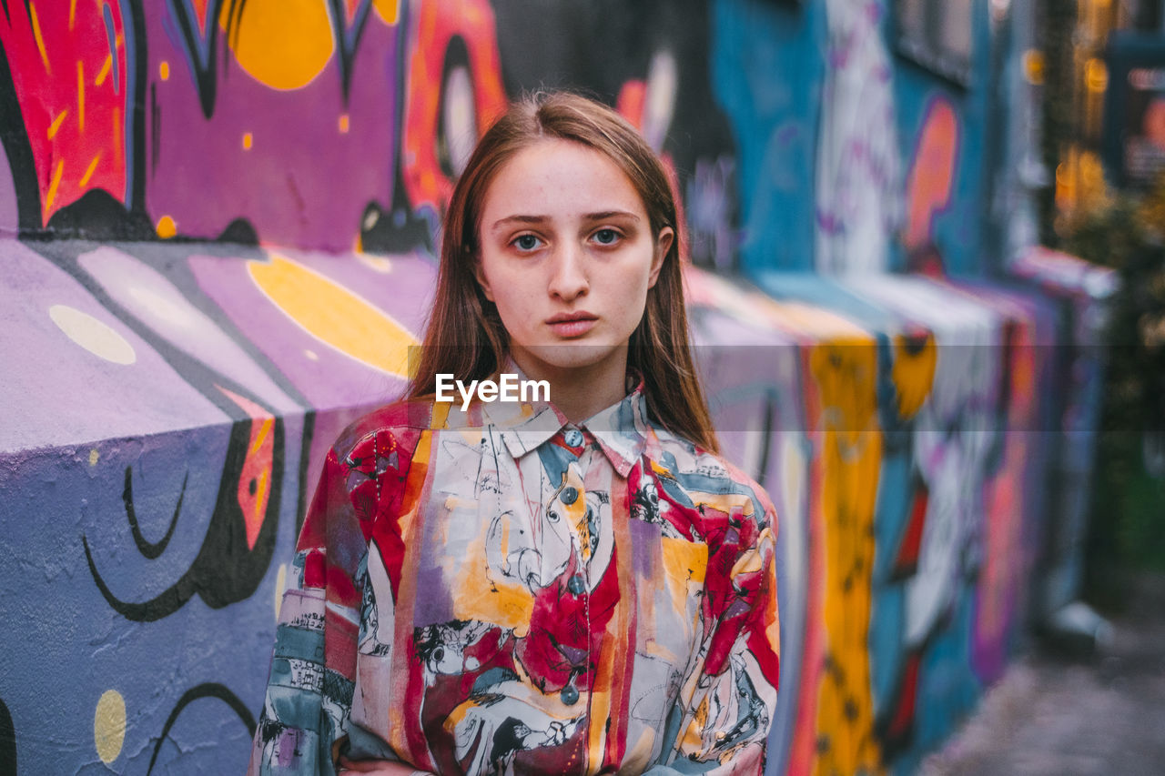 Portrait of young woman standing against graffiti