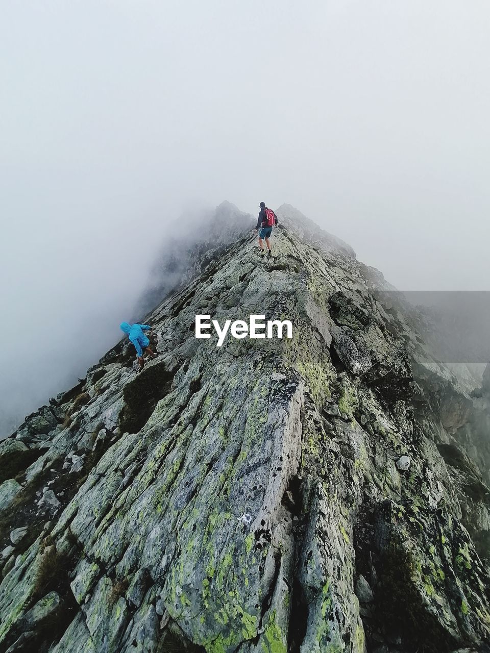 MAN ON ROCKS AGAINST MOUNTAINS