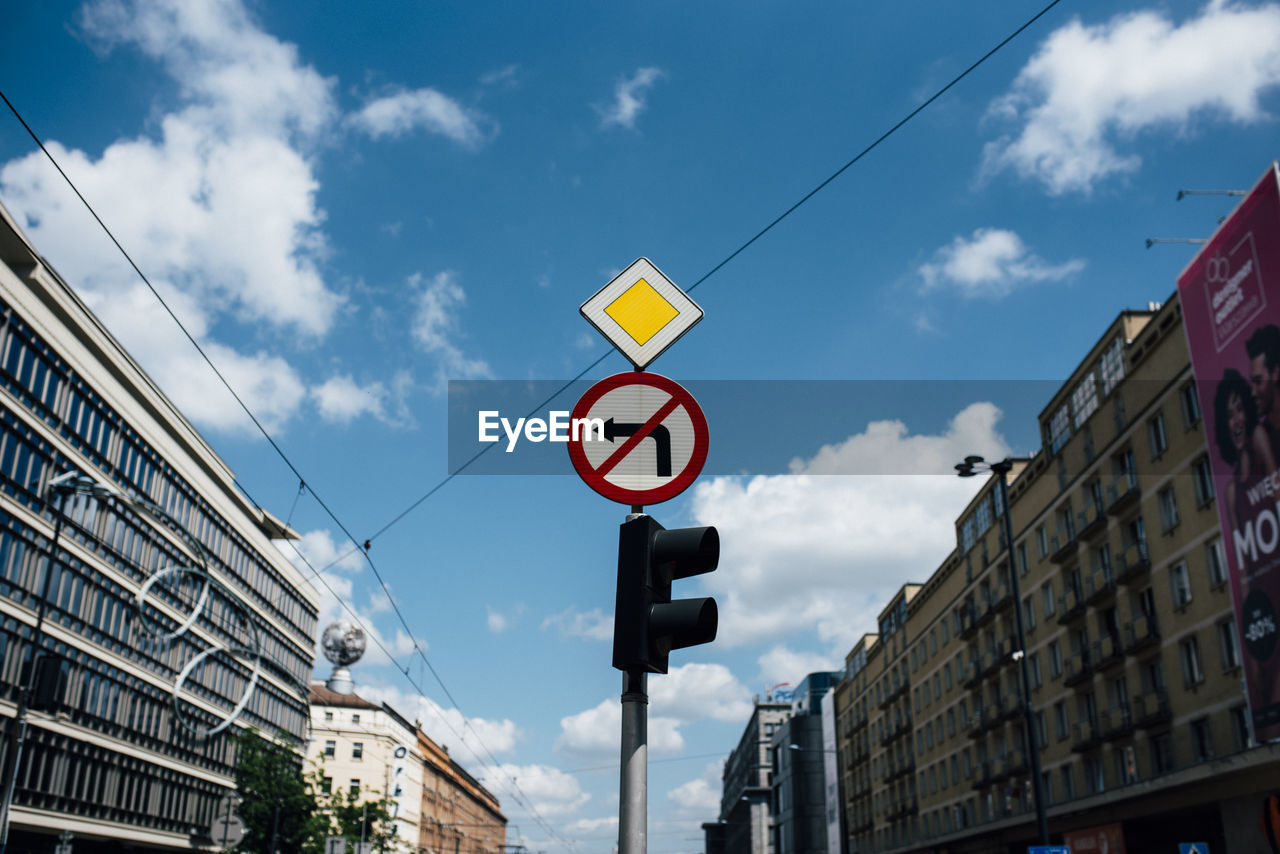 Low angle view of road sign by buildings against sky