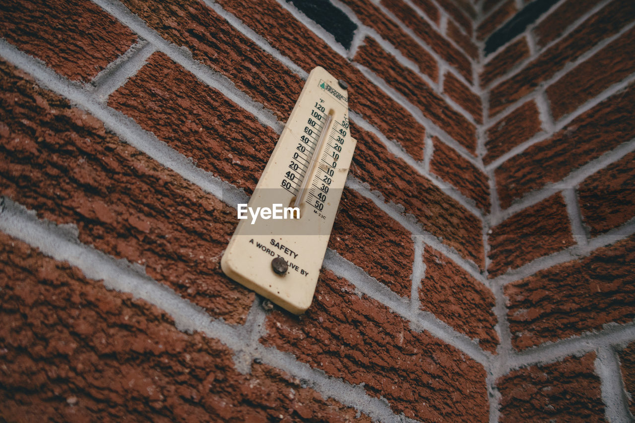 Looking up at thermometer on brick wall.