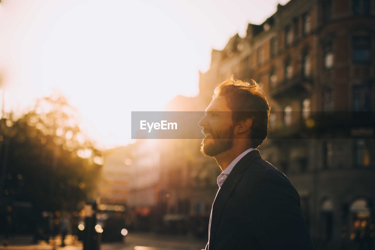 Side view of smiling man standing against sky in city