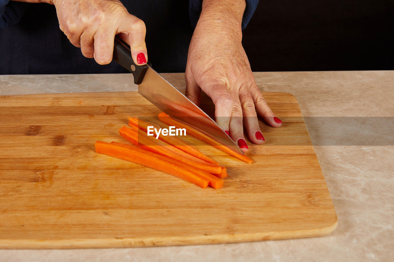 hand, cutting board, one person, food and drink, food, indoors, wood, preparing food, adult, carrot, chopping, kitchen knife, kitchen, cutting, healthy eating, freshness, vegetable, wellbeing, domestic room, home, occupation, root vegetable, holding, produce, domestic kitchen, lifestyles, raw food, chef, men, floor, high angle view, close-up, table, skill, domestic life, kitchen counter, baked