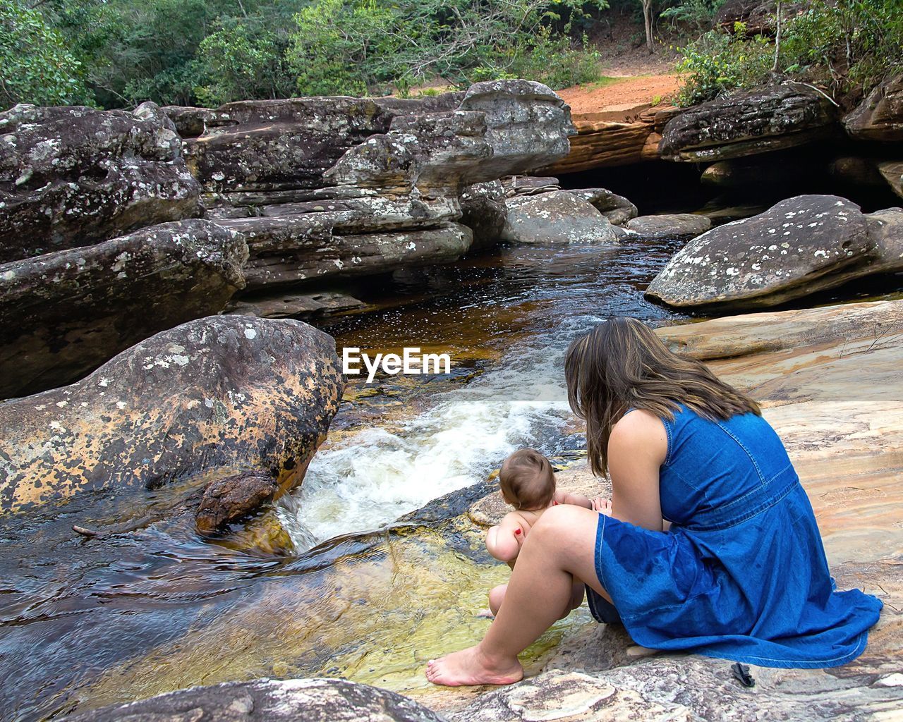 Side view of woman holding daughter by stream in forest