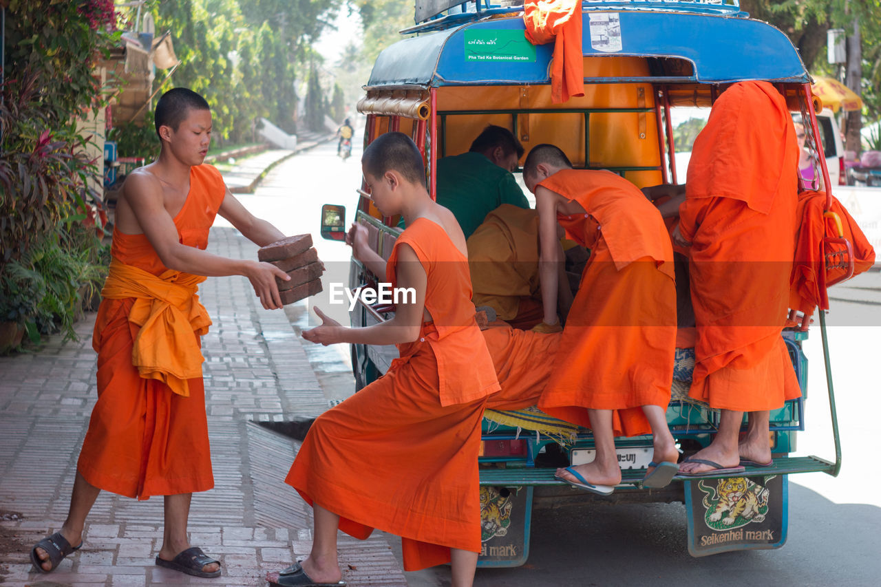 monk, adult, orange color, men, group of people, clothing, women, full length, transportation, religion, childhood, child, city, person, traditional clothing, mode of transportation, vehicle, togetherness, street, belief