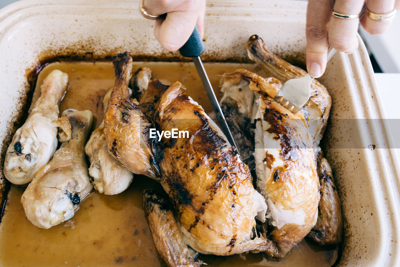 Cropped hands cutting roast chicken in container