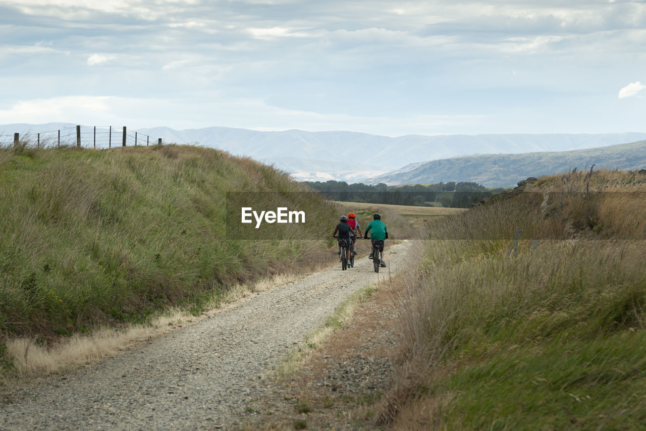 REAR VIEW OF MEN WALKING ON ROAD AGAINST SKY