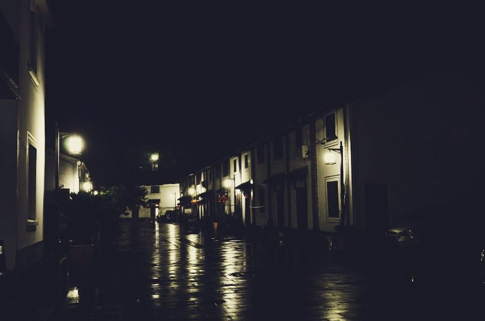 Wet street amidst illuminated houses at night