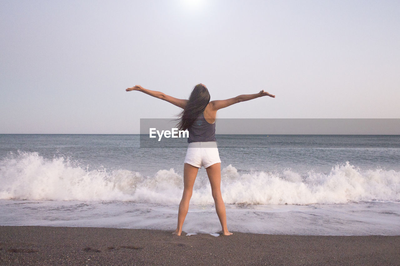 Rear view of woman with arms outstretched standing at beach