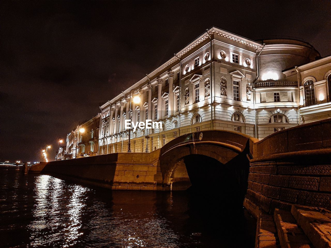 LOW ANGLE VIEW OF ILLUMINATED BRIDGE OVER CANAL