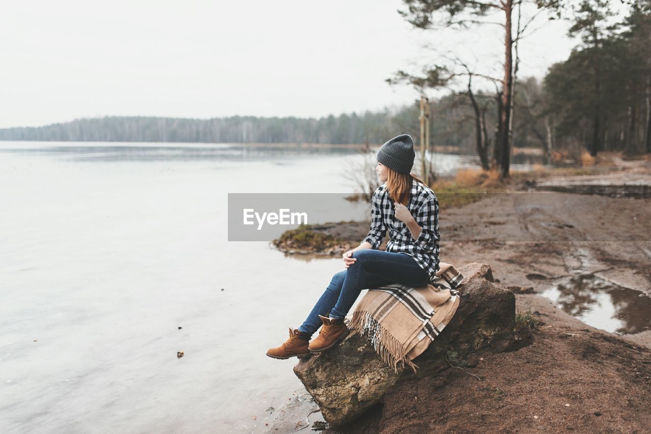 Woman sitting by lake against sky