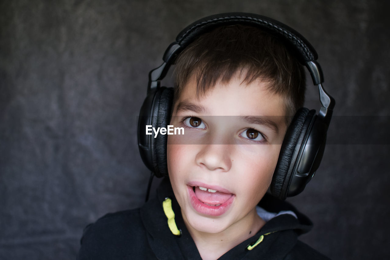 Close-up of boy listening music in headphones against wall