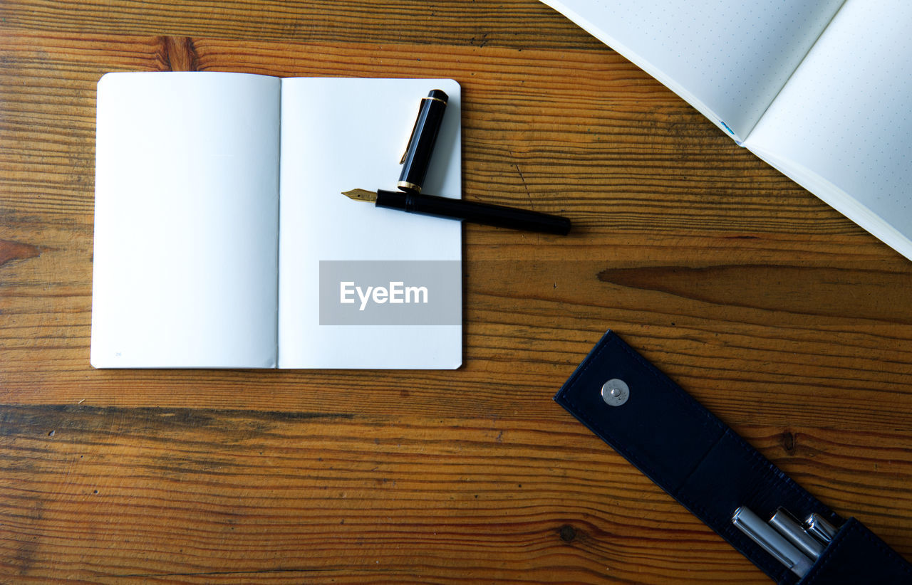 Paper notebook, fountain pen and ink on wooden table - flat lay