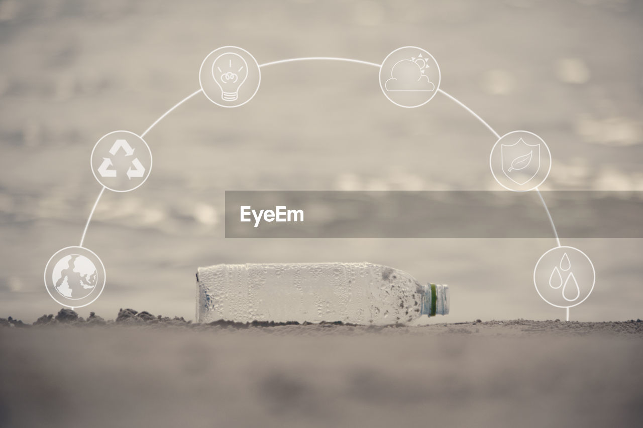 Digital composite image of icons over bottle at beach