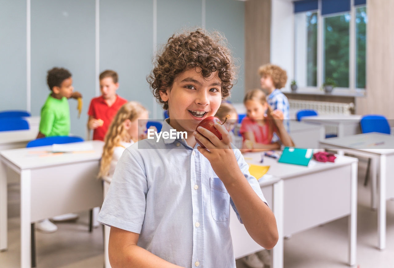 Portrait of boy eating apple at classroom