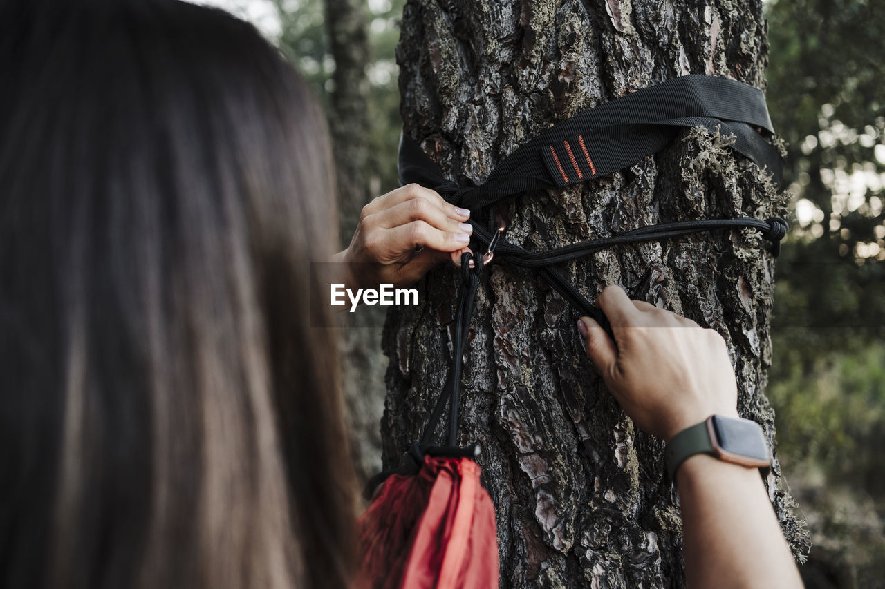 Young woman adjusting hammock to tree in forest during vacation