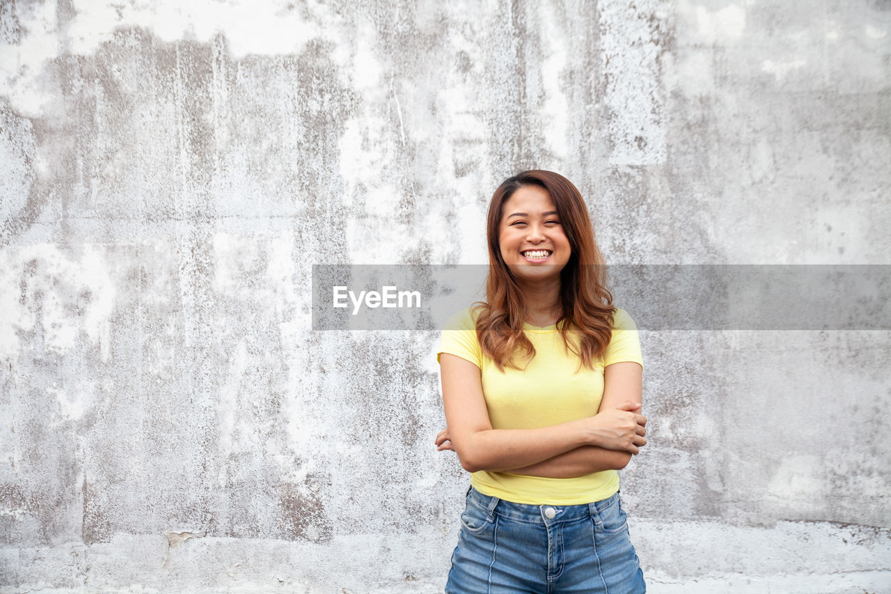 Portrait of smiling young woman standing against wall