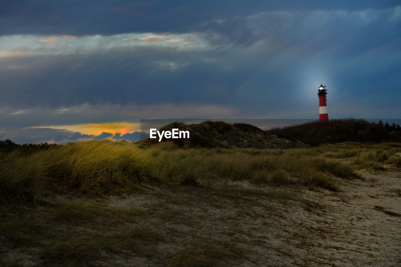 Lighthouse on field against sky at sunset