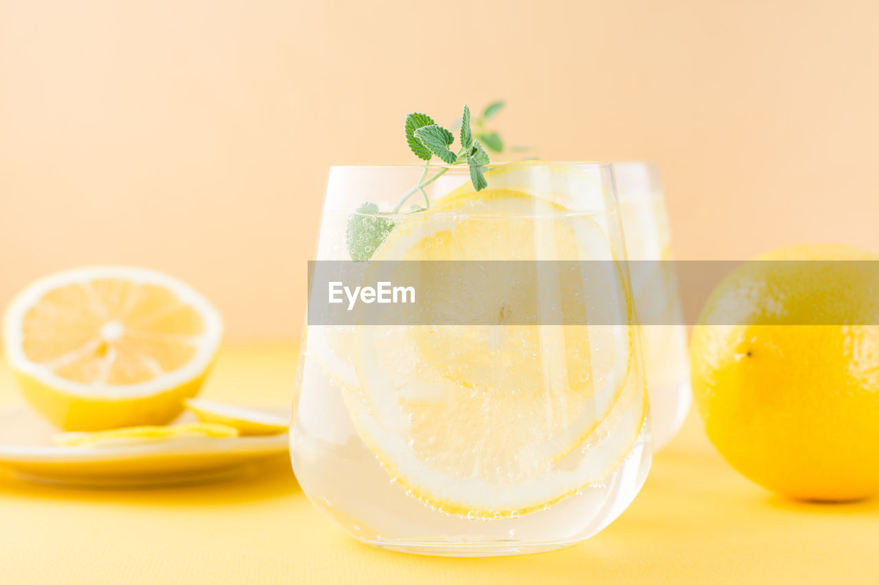 Sparkling water with lemon, melissa and ice in glasses and lemon slices on a saucer on a yellow 