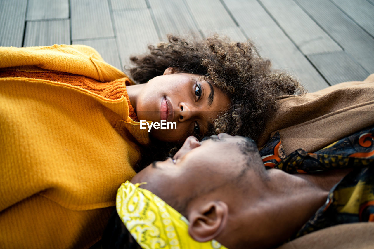 Top view of trendy african american man and woman in bright coat lying opposite with face to face looking at each other