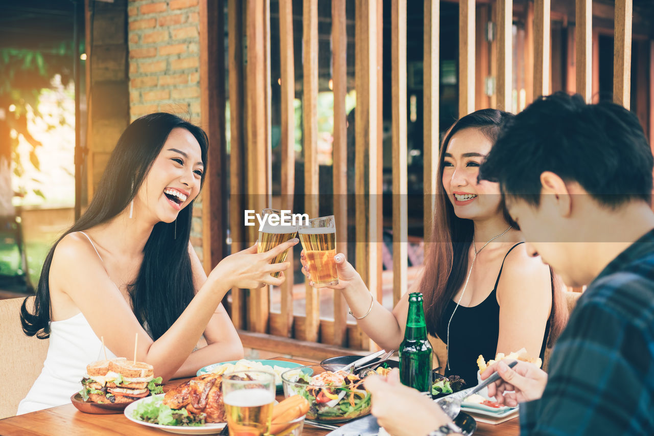 Cheerful friends drinking beer on table at restaurant