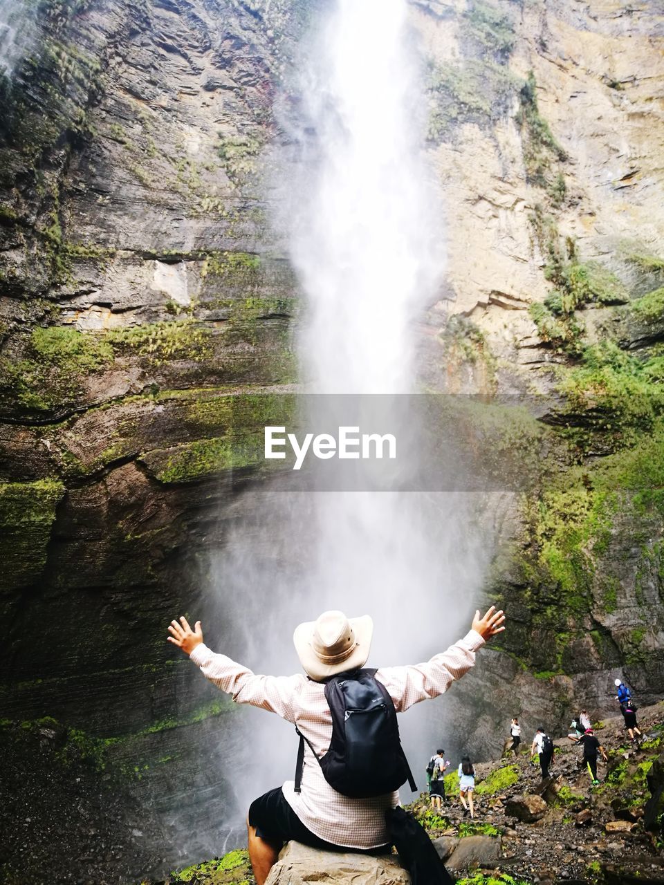 Rear view of man with arms outstretched looking at waterfall