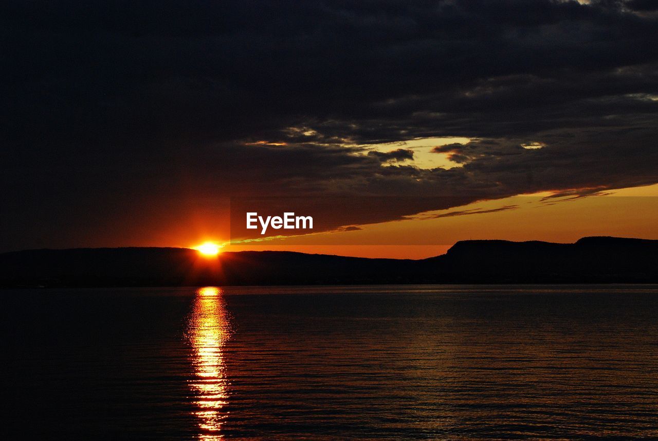 Scenic view of sea against dramatic sky during sunset