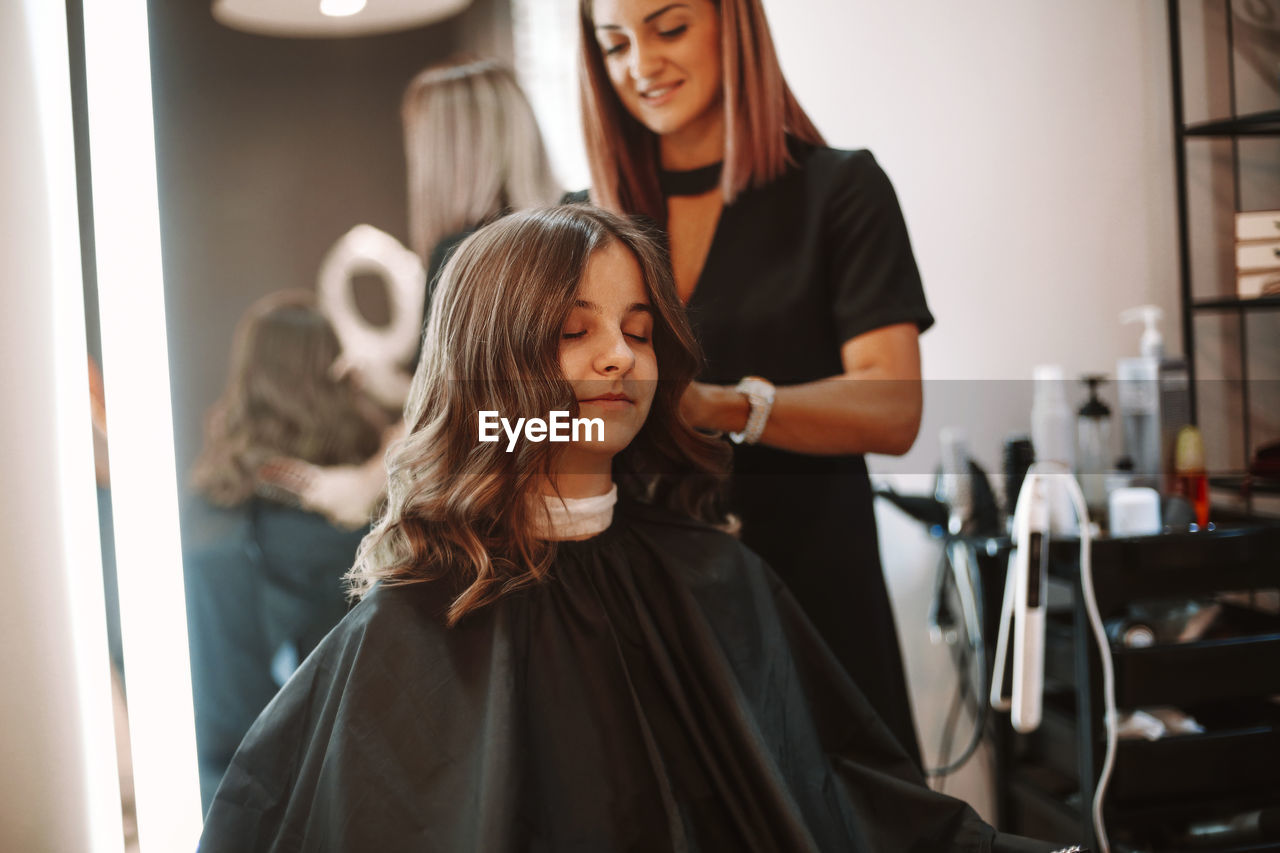 Smiling barber cutting hair of girl at salon