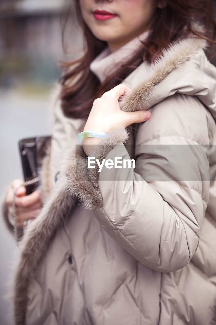 MIDSECTION OF WOMAN HOLDING SMART PHONE IN SNOW