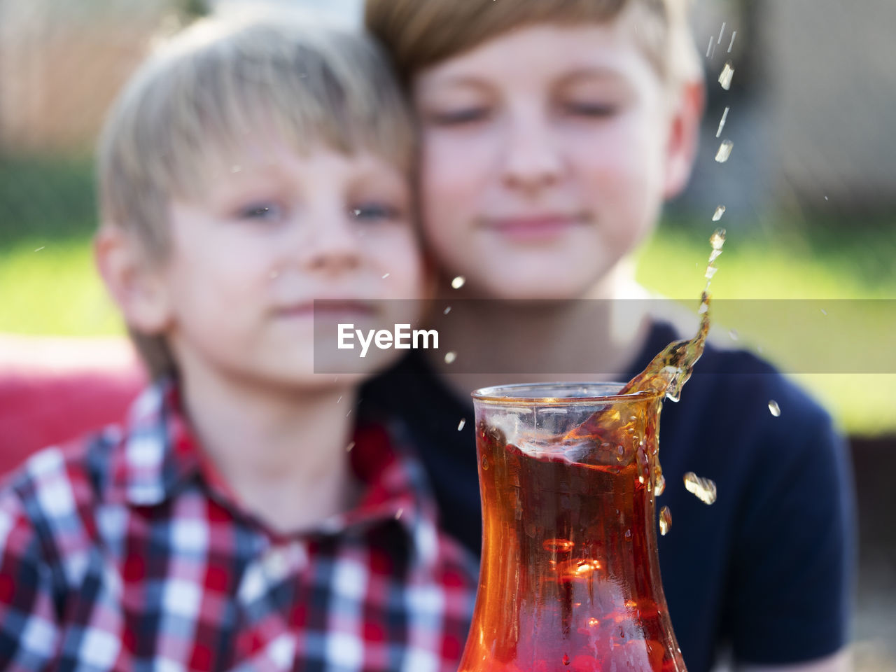 Two caucasian boys watches a splash of tea in a cup from a falling piece of sugar