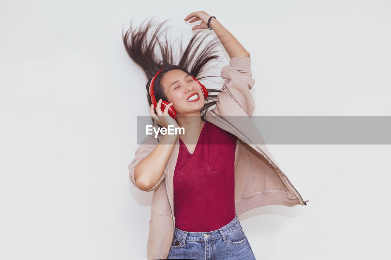 YOUNG WOMAN STANDING AGAINST WHITE WALL