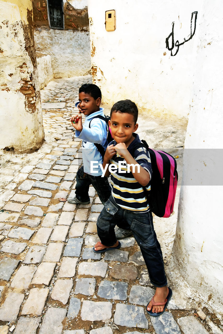 FULL LENGTH PORTRAIT OF BOY STANDING ON COBBLESTONE