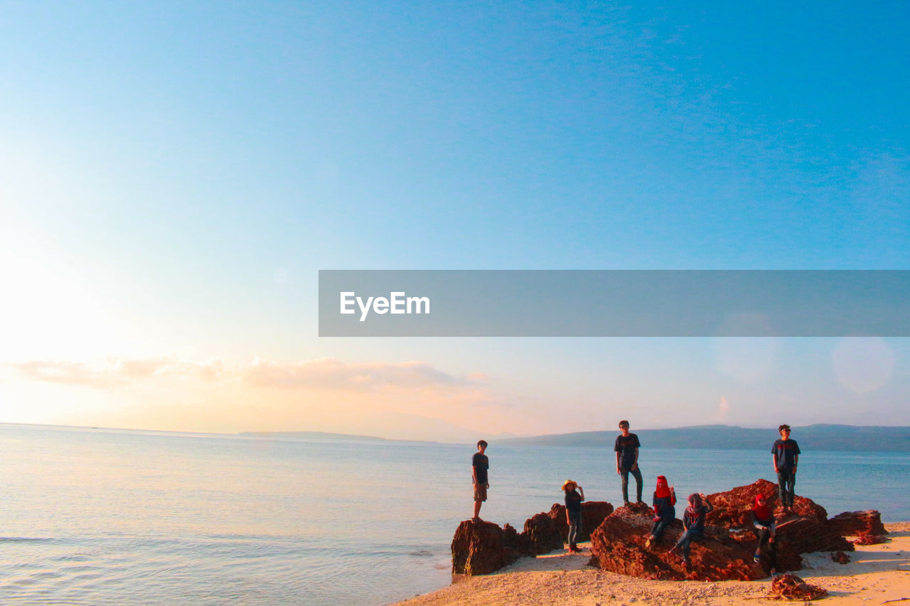 People on rocks at beach against sky