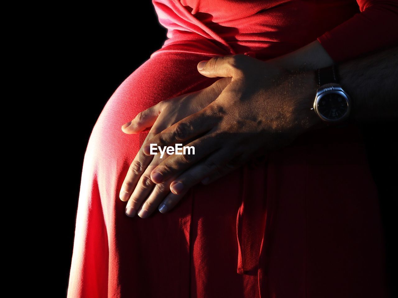Cropped hand of man touching pregnant woman stomach against black background