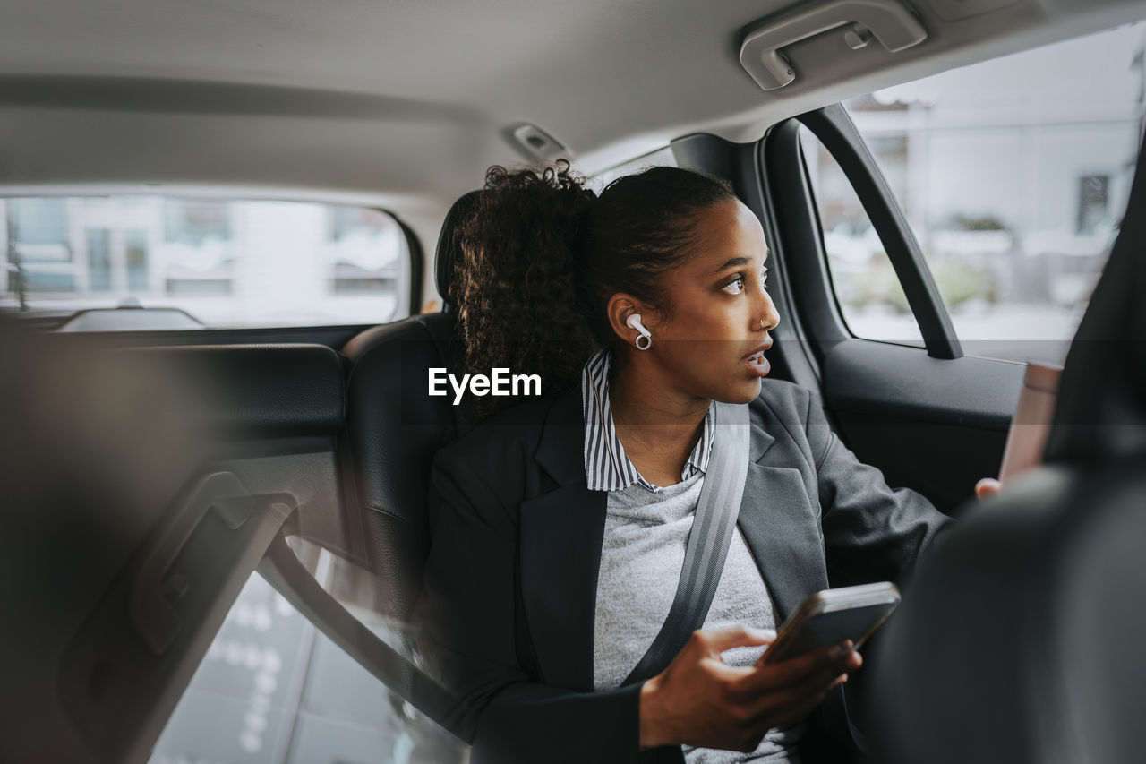 Businesswoman looking through window and talking on smart phone while sitting in car