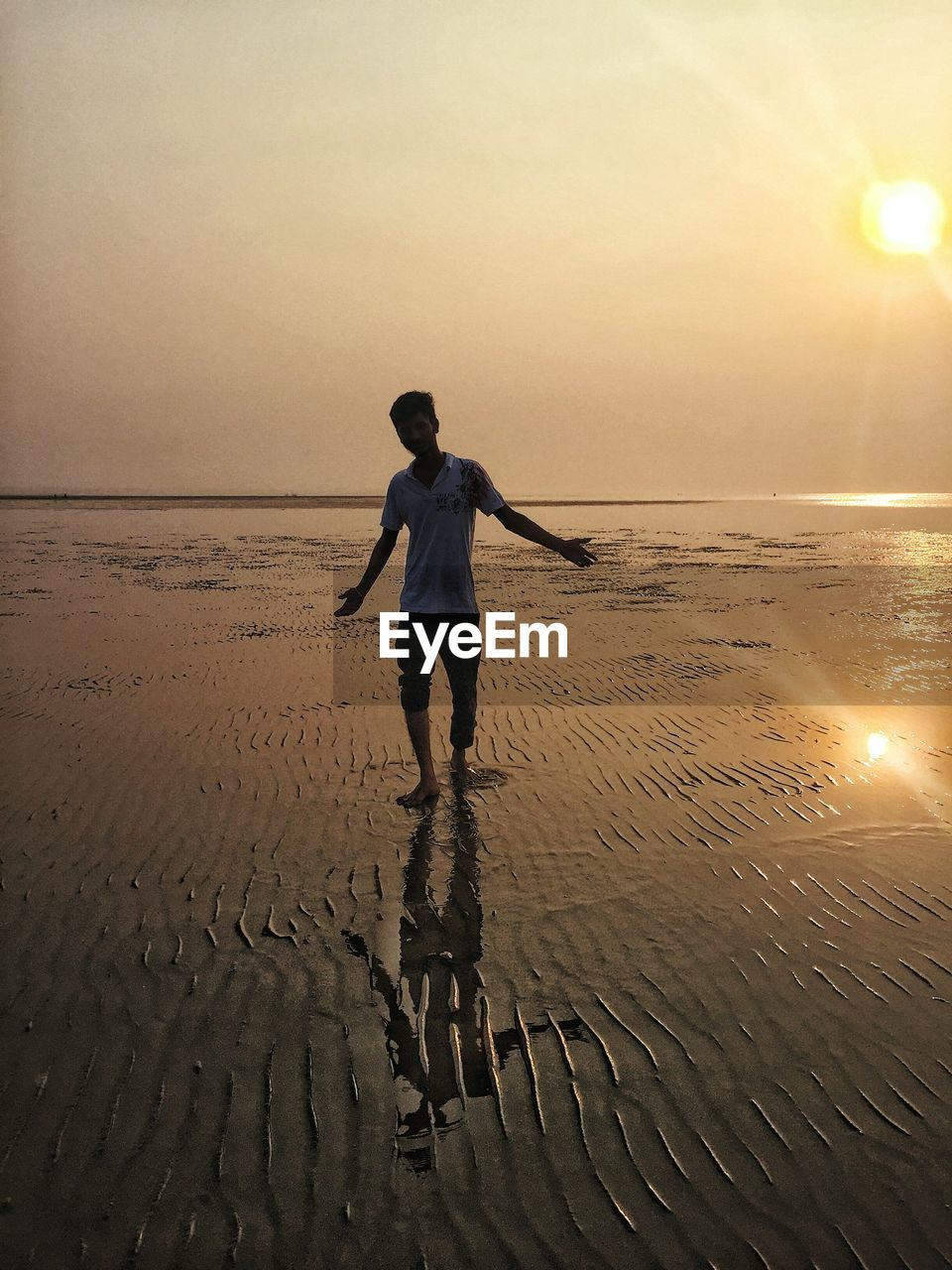 Full length of man standing on beach against sky during sunset