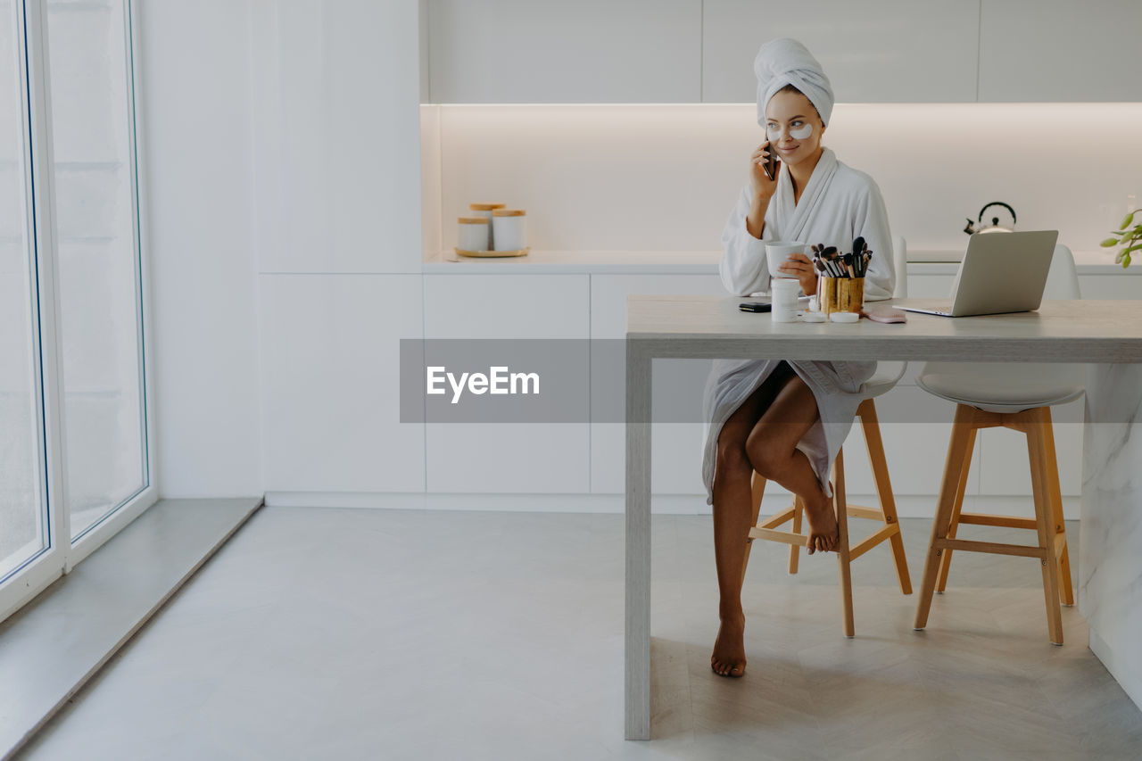 Smiling woman with eye patch talking on phone while holding coffee cup at home