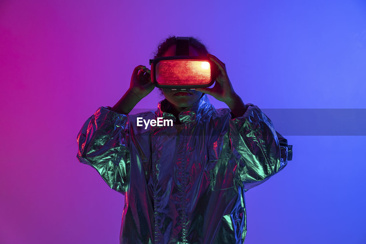 Woman wearing virtual reality simulator standing against multi-colored background