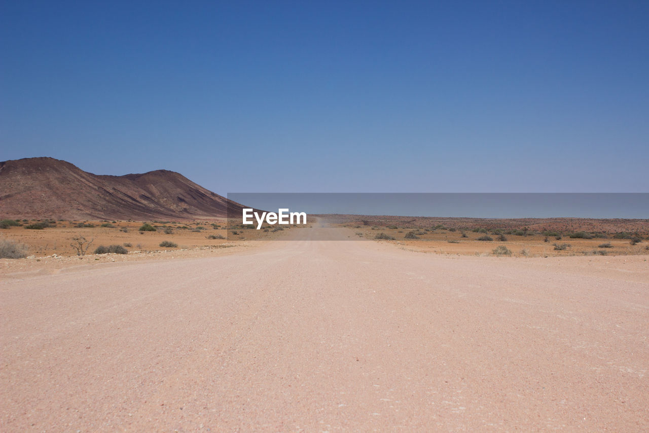 Scenic view of desert road against clear sky