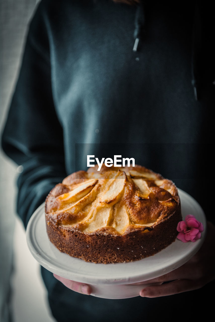 Crop anonymous housewife in black wear holding plate with yummy homemade freshly baked aromatic apple cake