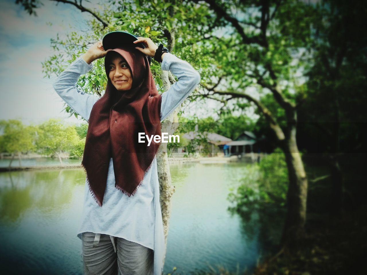 PORTRAIT OF SMILING YOUNG WOMAN STANDING AGAINST TREES