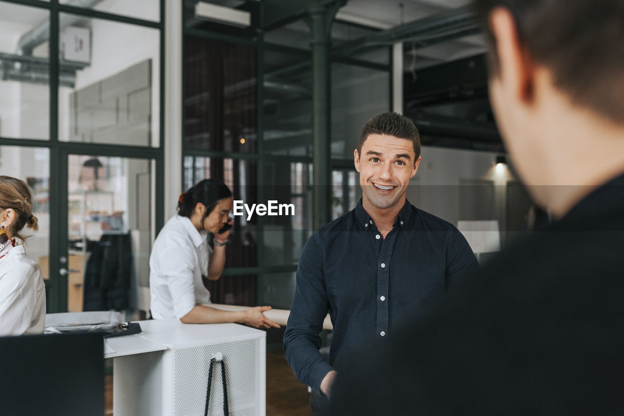 Smiling businessman looking at male colleague at office