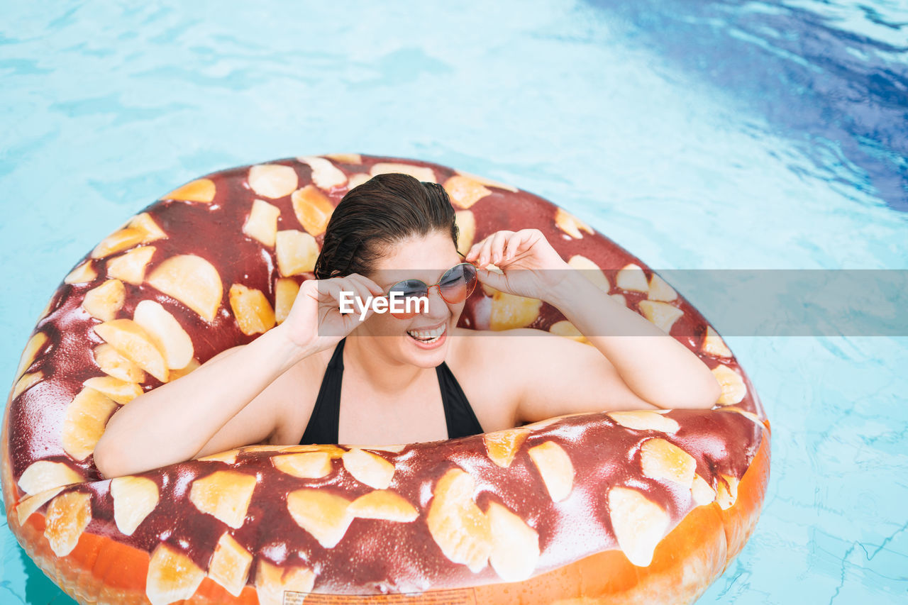 Happy young woman plus size body positive in inflatable doughnut circle swimming in pool