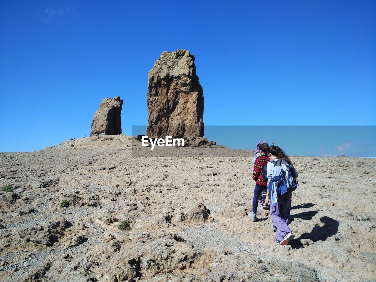 Rear view of people walking on rock formation against blue sky