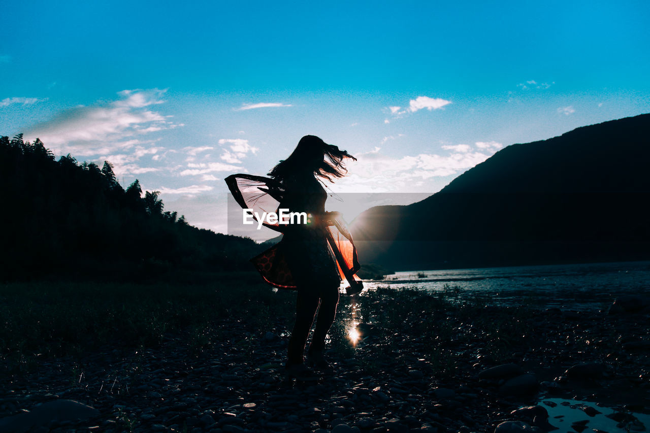 Woman holding scarf on field against blue sky during sunset