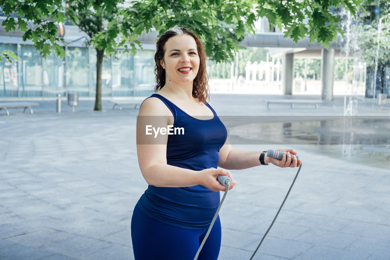 Confident plus size curvy happy young woman doing exercise workout with skipping rope outdoors.