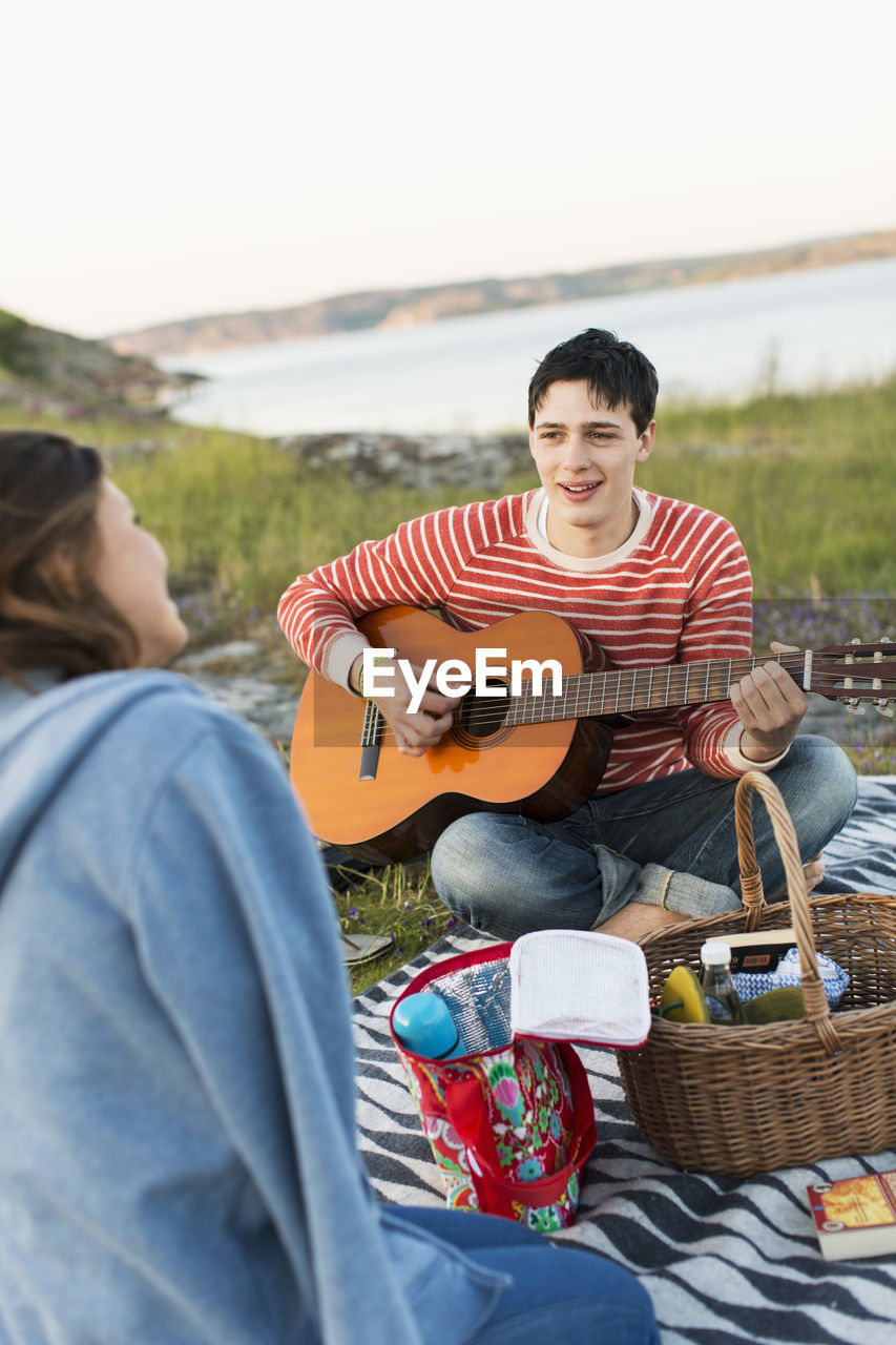 Man playing guitar for girlfriend while enjoying picnic on field