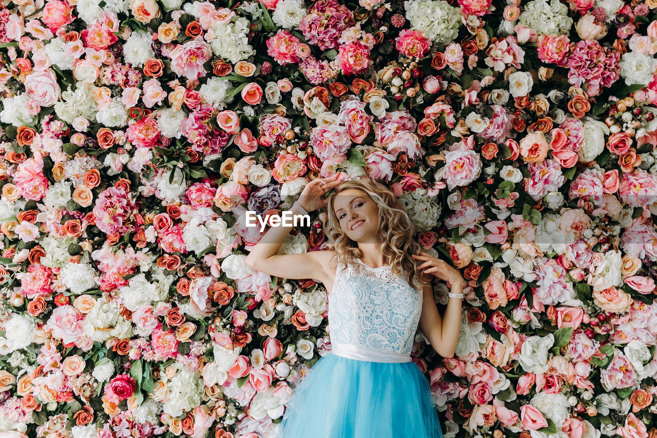 Young woman wearing blue dress standing against flowering plants